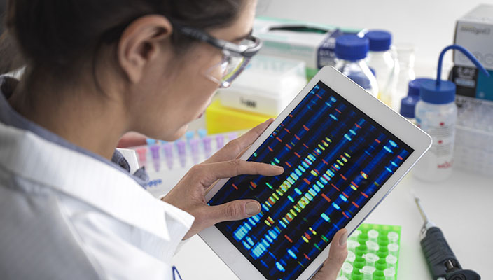 A lab specialist reviews DNA results on a tablet.