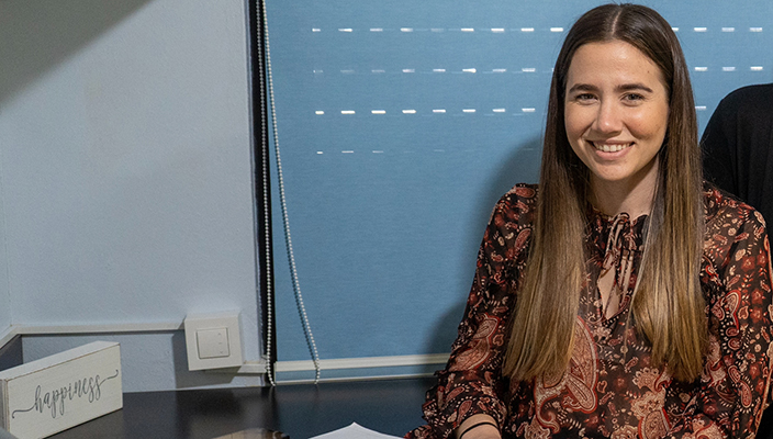 La doctora Normarie Torres-Blasco está sentada frente a un escritorio. Está miranda a la cámara y sonriendo.