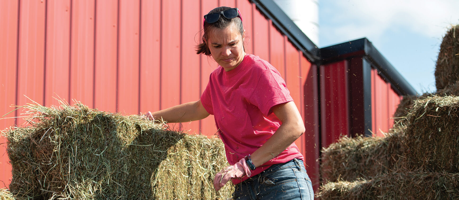 Person moving bales of hay in front of a barn