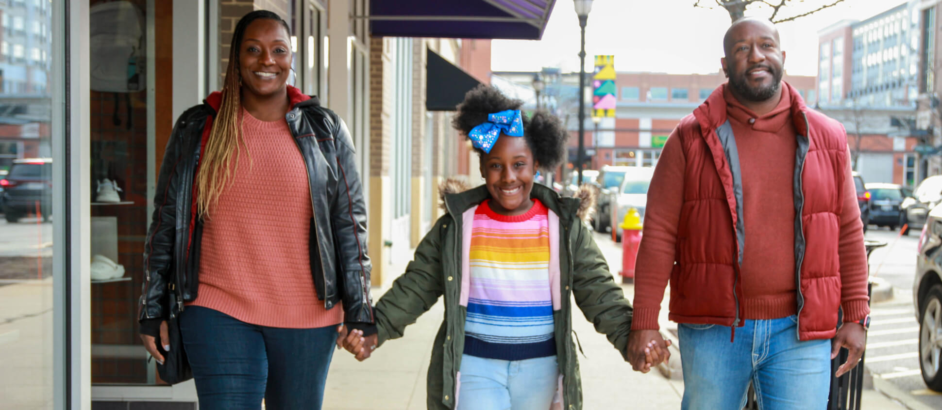 Family of three walking towards the camera while holding hands