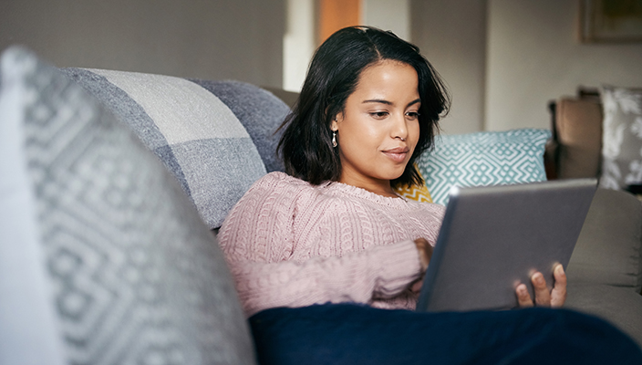 Woman reading from a tablet and sitting on the couch in a living room. 