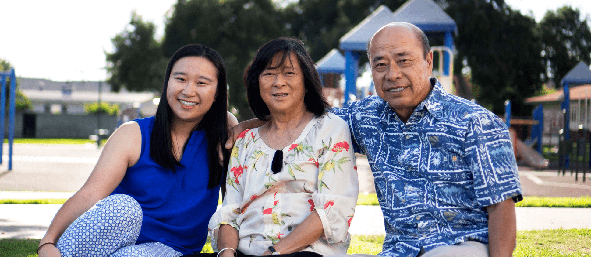 Family of three sitting together in a park.