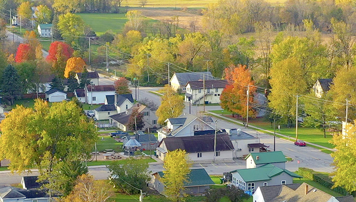 An aerial photo of a neighborhood shows several houses, big green trees, and a street.