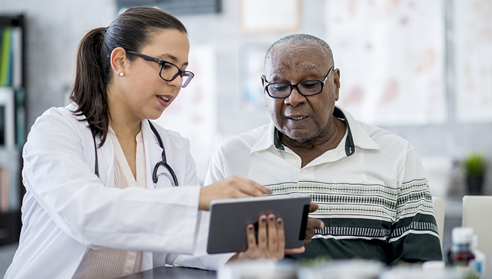 A doctor shares information in a tablet with a patient, an older person. 