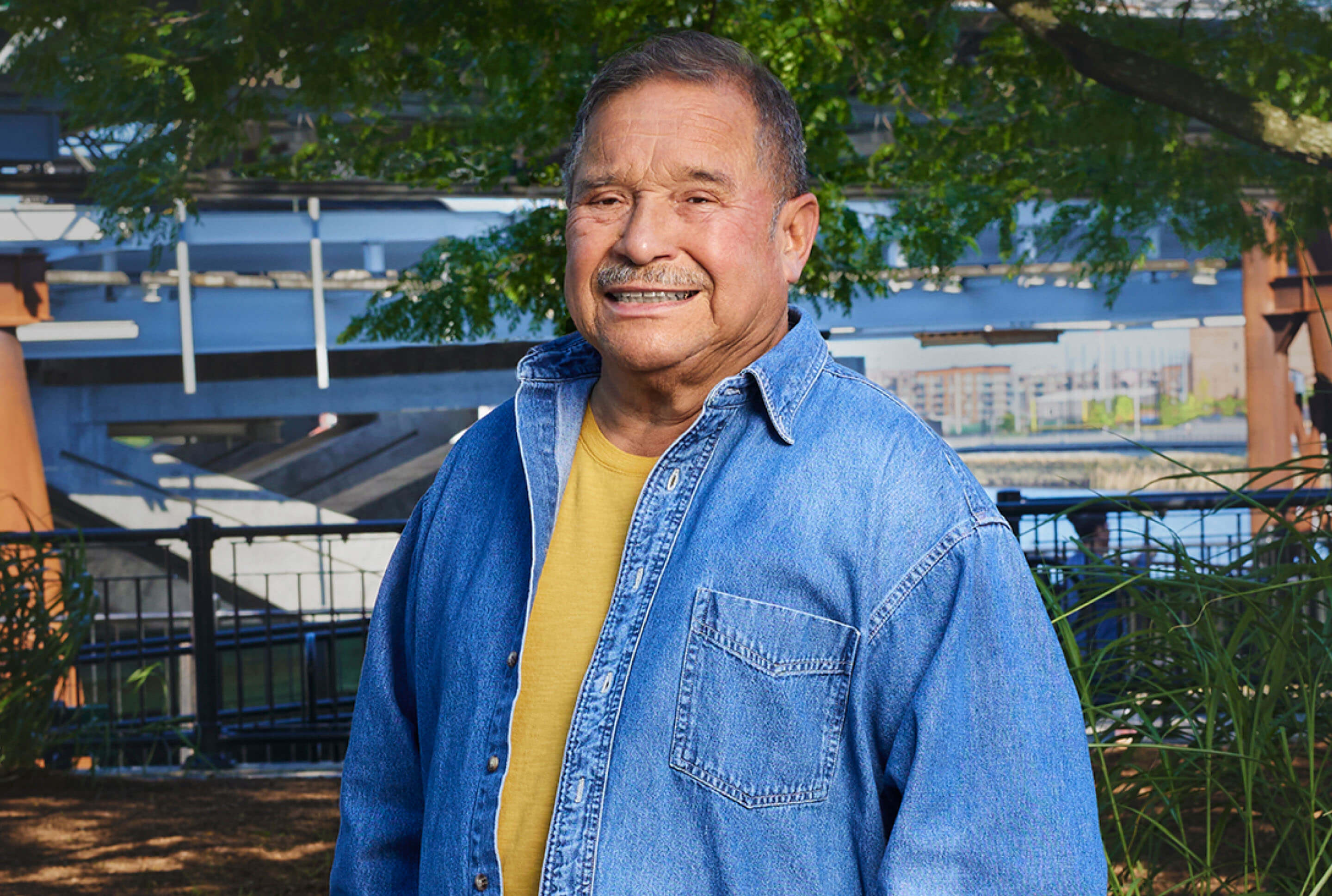 A man in a denim shirt standing in front of a tree.