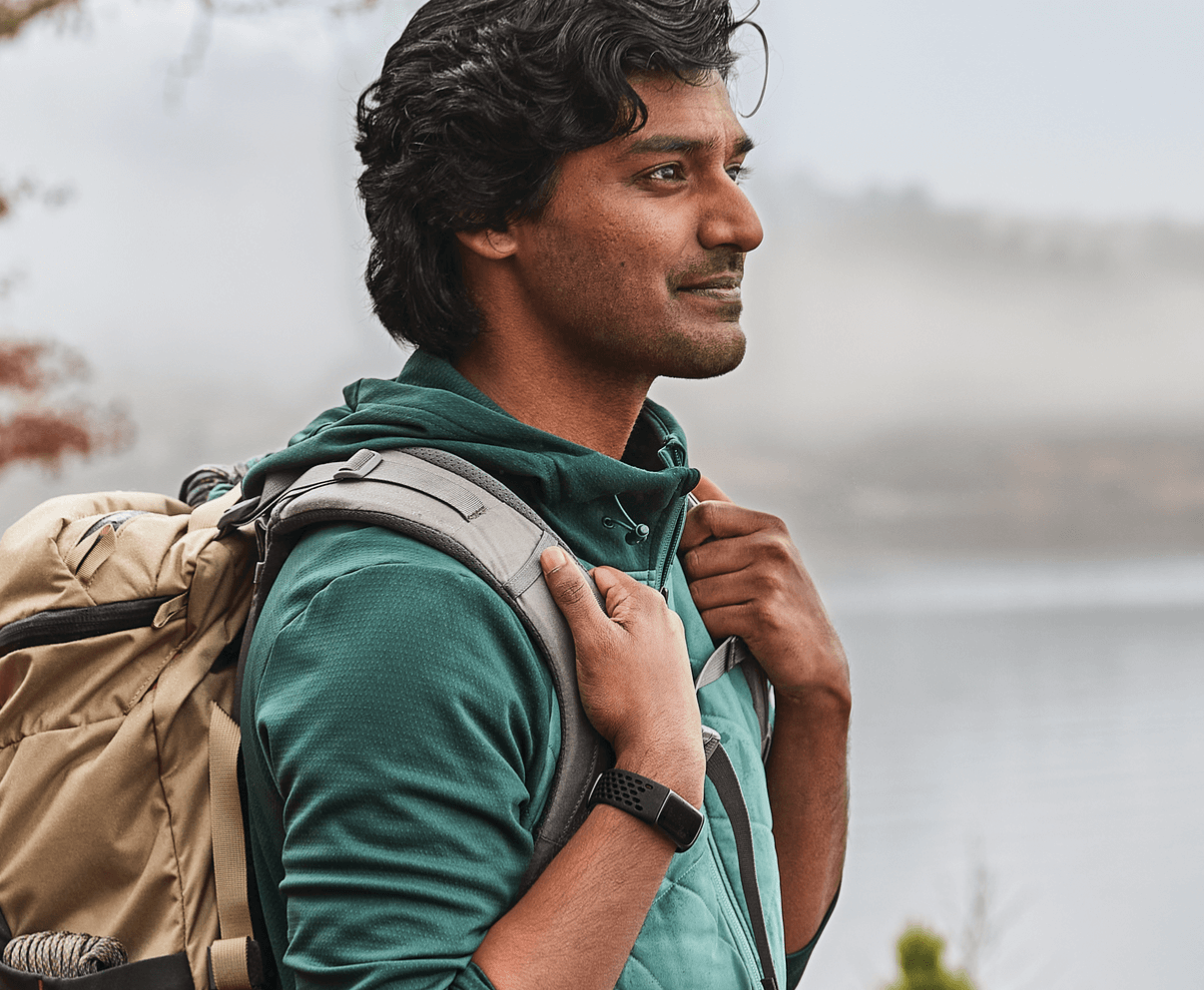 A man with a backpack standing next to a lake.